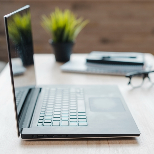 Open laptop on a wooden desk with a green potted plant and glasses in the background